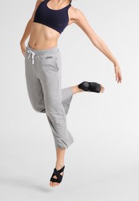 Szare spodnie dresowe o szerokich nogawkach i regulowanym pasie, zestawione z granatowym biustonoszem sportowym oraz czarnymi butami do tańca z krzyżującymi się paskami.