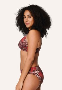 Bikini a stampa leopardata con dettagli floreali rossi. Top a bralette e slip a vita alta. Tessuto liscio con un design aderente.