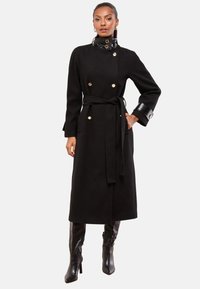 Sort uldfrakke med dobbeltradet design, guldknapper, bælte i taljen og en blank sort krave og manchetter.