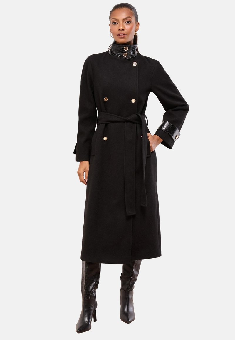 Sort uldfrakke med dobbeltradet design, guldknapper, bælte i taljen og en blank sort krave og manchetter.