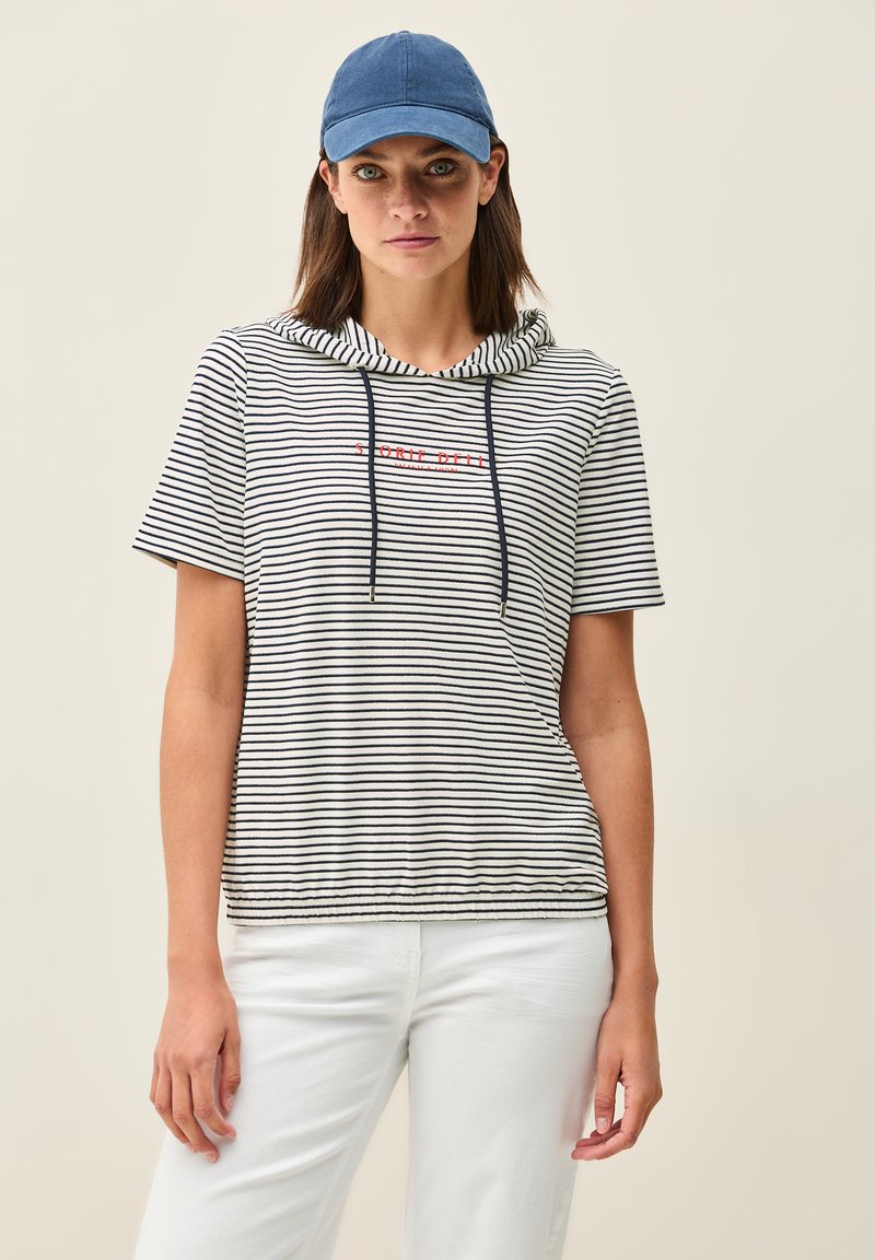 Sudadera de manga corta a rayas en blanco y azul marino con texto rojo. Presenta cordones y dobladillo elástico. Combinada con pantalones blancos y una gorra azul.