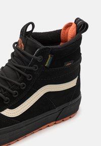 Sorte semsket høyhælte sneakers med oransje hæltab og kremfarget side stripe. Har metallhull og strukturert sort gummisåle.