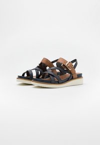 Schwarze und braune Leder-Sandalen mit einem Kreuzriemendesign, verstellbarem Schnallenverschluss, gepolstertem Fußbett und weißer Gummisohle.