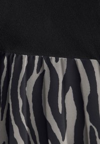 Czarna prążkowana tkanina przechodzi w płynącą tkaninę z czarno-szarym wzorem zebry.