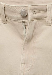 Pantalones de algodón beige con cierre de cremallera y botón de metal. Incluyen trabillas para cinturón y un sutil patrón de tela texturizado.