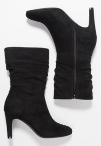 Bottines à talon en daim noir avec un design décontracté, un bout pointu et une fermeture éclair latérale. Matière texturée et talon brillant en accent.