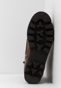 Botte marron avec une semelle en caoutchouc noir robuste dotée de profondes crampons. Tige en suède doux avec un design latéral texturé et une fermeture éclair sur le côté.