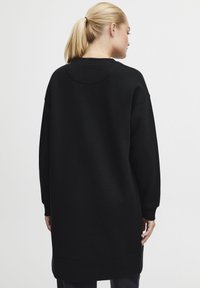 Svart oversized sweatshirt med rund hals, långa ärmar och en texturerad yta, med en lätt böjd fåll i ryggen.