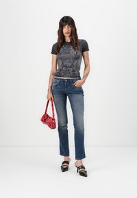 Juodas grafikos t-shirt'as, mėlyni tiesūs džinsai, juodos aukštakulnės sandalai ir maža raudona rankinė su gėlių raštu.