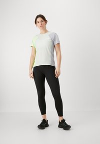 Grå og neon grønn treningst-skjorte med korte ermer, kombinert med svarte tights og svarte joggesko, med en tettsittende design.