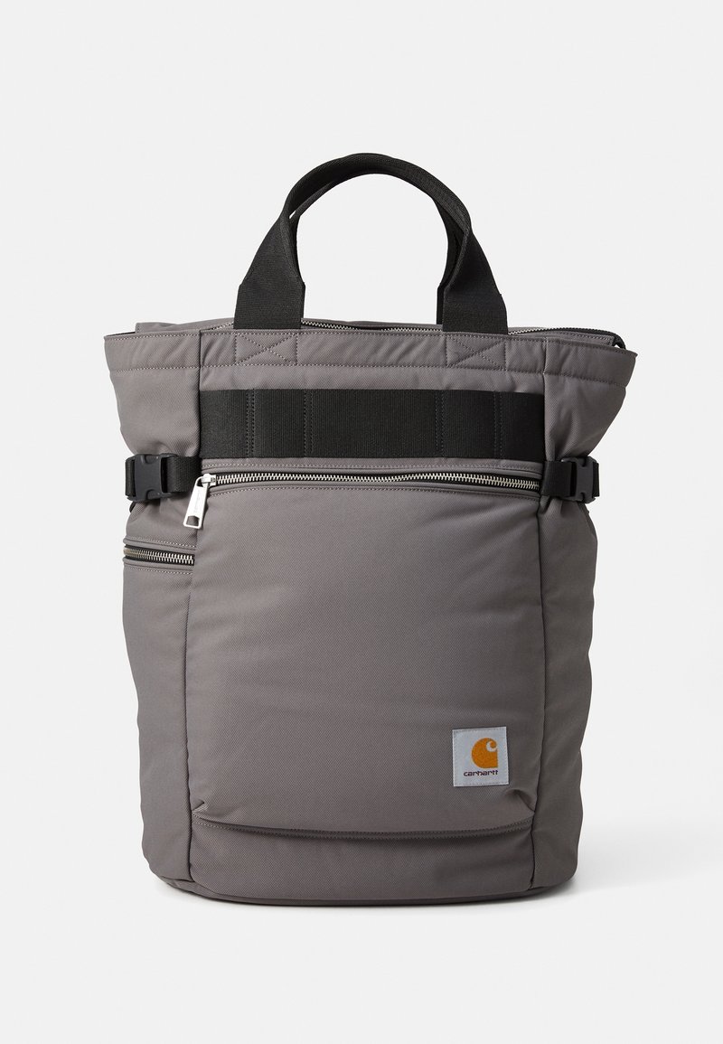 Sac fourre-tout gris Carhartt avec poignées noires, poche avant zippée, sangles latérales à boucle et petit patch logo de la marque en bas devant.