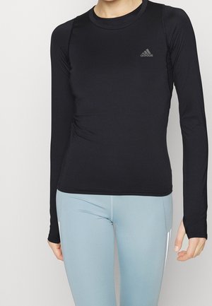 Person wearing a fitted black long-sleeve Adidas shirt paired with light blue athletic leggings against a plain background.