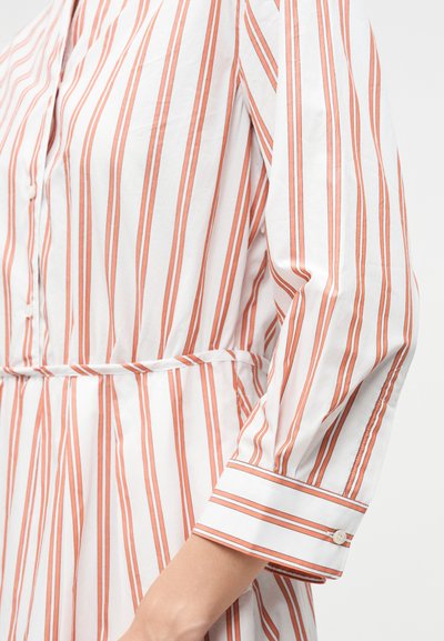 Λευκό μακρυμάνικο πουκάμισο με κάθετες πορτοκαλί και καφέ ρίγες, με κουμπωτά μανίκια και ζώνη στη μέση.
