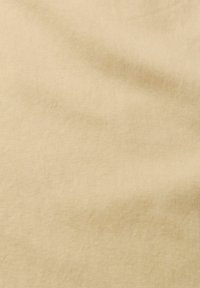 Tissu beige uni montrant de doux plis et une texture subtile, sans motifs ni objets visibles.