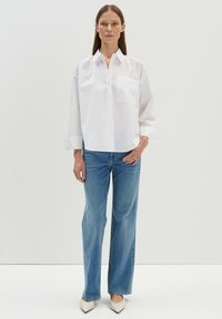 Camicia bianca a maniche lunghe con taschino sul petto, abbinata a jeans dritti azzurri e décolleté beige a punta. Tessuto di consistenza liscia.