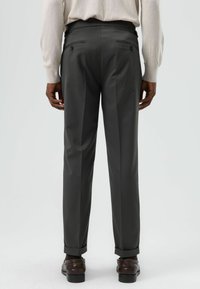 Op maat gemaakte grijze broek van soepel materiaal, met een gestroomlijnde pasvorm, twee achterzakken en omgeslagen pijpen. Geschikt voor formele gelegenheden.