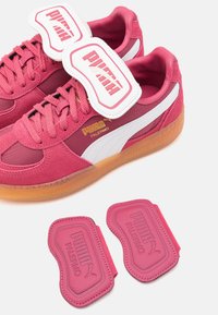 Lyserøde ruskinds sneakers med hvide detaljer, gummisåler og guldlogo. Inkluderer to aftagelige lyserøde tags med logo.
