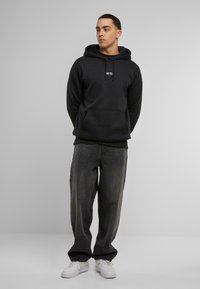 Felpa nera con tasca frontale a marsupio e cordino regolabile. Indossata con jeans grigi scuri a vestibilità comoda e sneakers bianche.
