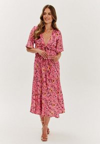 Ružové kvetinové mididress s krátkymi rukávmi, hlbokým výstrihom do V, viazaním v páse, splývavým materiálom a farebnými vzormi na svetlom pozadí.