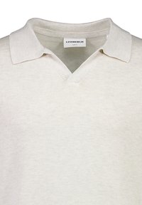 Ljusbeige polo med smal passform, med V-hals och en mjuk ribbad krage. Tillverkad av textil med subtila detaljer.