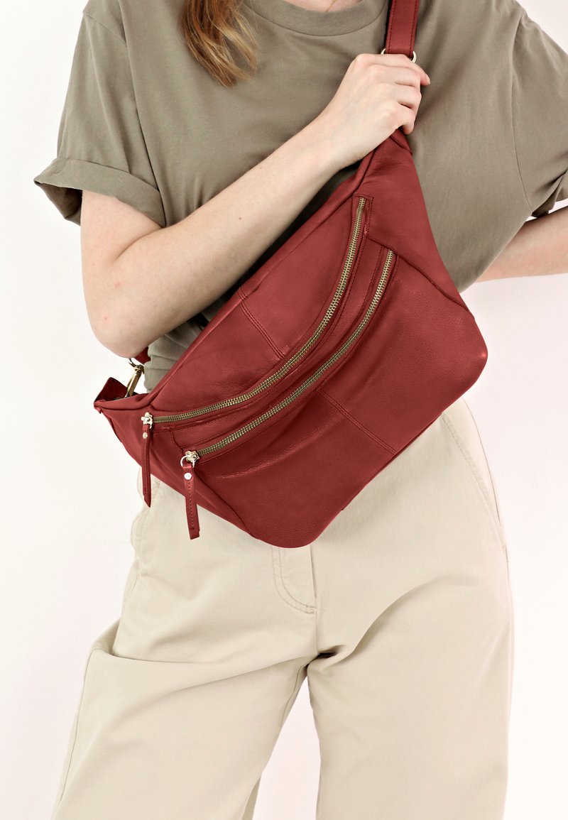 Borsa a tracolla in pelle borgogna con tre tasche con zip, una forma curvata e una texture liscia. Cinghia regolabile attaccata al lato.