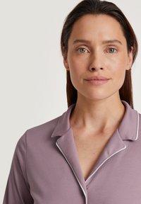 Light purple top with a collar, featuring white piping. Smooth texture, fitted design. Model has straight hair and neutral makeup.