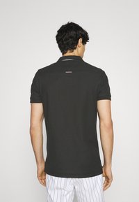 Svart pikétröja med krage, korta ärmar och en rosa detalj på baksidan. Tyget ser slätt och lätt ut. Avslappnad passform.