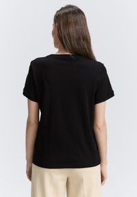 Zwarte T-shirt met korte mouwen, een ronde hals, een gladde textuur en een ontspannen pasvorm. De achterkant toont een eenvoudig, onopgesmukt ontwerp.