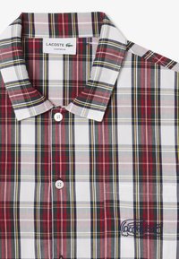 Rövid ujjú kockás ing fehér, piros, zöld és sárga árnyalatokban. Gombbal rögzített gallérral és hímzett logóval a mellzseben.