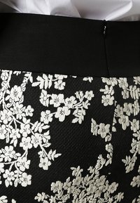 Czarna spódnica z teksturowanej tkaniny, z białym haftem kwiatowym i jednolitą czarną talią.