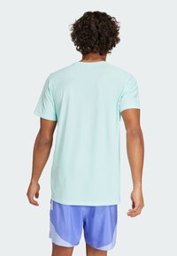 T-shirt bleu clair à col rond, fabriqué à partir d'un tissu respirant, avec des manches courtes et une coupe décontractée. Porté avec un short de sport violet.