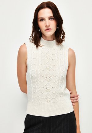 Gebreide mouwloze sweater in crème met geribde kraag, textuur van diamantpatronen en kleine parelaccenten. Aansluitend silhouet.