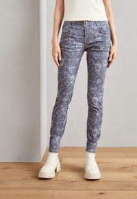 Tajta, mönstrade jeans i ljusblått med intrikata blommönster, i kombination med rejäla vita platåstövlar. Material av bomullsblandning.