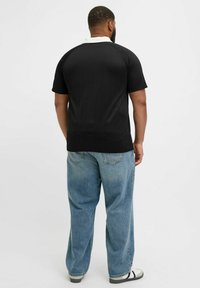 Svart texturerad polotröja med vit krage, parat med ljusblå löst sittande jeans och sandaler. Tröjan har en ribbad design.