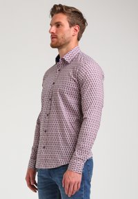 Camisa de botones con un patrón geométrico en tonos de rosa y lavanda, de manga larga y cuello con solapas.