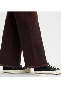 Jeans burdeos de pierna ancha con dobladillos deshilachados, combinados con zapatillas negras de caña baja con suelas y cordones blancos.