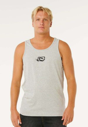 Blond mand står med front mod kameraet iført en grå tanktop med en lille sort grafik på brystet og mørke bukser.