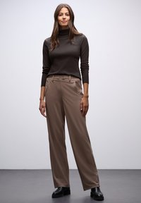 Brązowy golf zestawiony z beżowymi spodniami o szerokich nogawkach z bocznymi kieszeniami i paskiem, uzupełniony czarnymi botkami za kostkę.