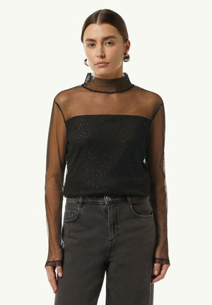 Schwarzes Netzoberteil mit langen Ärmeln, hohem Kragen und glänzenden Akzenten, mit einem taillierten Oberteil und transparenten Ärmeln. Kombiniert mit dunklen Jeans.
