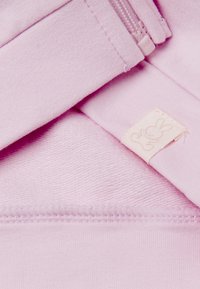Primo piano di un tessuto rosa con cerniera visibile, cuciture, e un piccolo etichetta con un semplice contorno di coniglio.