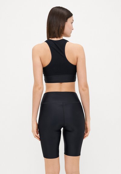 Črni športni modrček z zračnim mrežastim dizajnom, v kombinaciji s črnimi kratkimi hlačami do sredine stegna. Obe sta izdelani iz gladkega, raztegljivega materiala.
