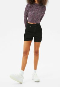 Svarta denimshorts med hög midja och framfickor, tillsammans med en långärmad, blommig crop top i nyanser av rosa och lila. Vita sneakers.