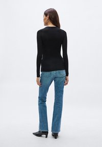 Zwarte top met lange mouwen, nauwsluitend, met een ronde halslijn; gecombineerd met blauwe jeans met rechte pijpen. Schoeisel met puntige neus en lage hak.