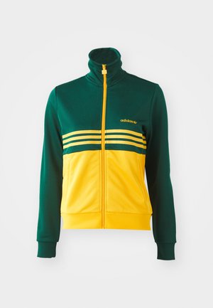 Casaco atlético com fecho de correr nas cores verde e amarelo, com um colarinho alto, apresentando três riscas horizontais e um logo dourado na parte superior esquerda.