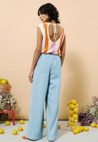 Häkeltop mit orange, rosa und weißen Streifen; offener Rücken mit Bindeband. Hellblaue, weit geschnittene gestreifte Hose; weiche Textur, lässige Passform.