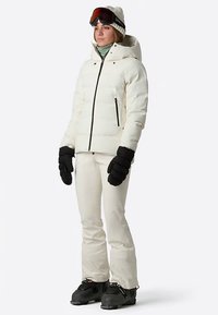 Weiße, isolierte Steppjacke mit Kapuze, schwarze Handschuhe und Skihose, getragen mit Skischuhen und Skibrille. Glatte Textur, minimalistisches Design.