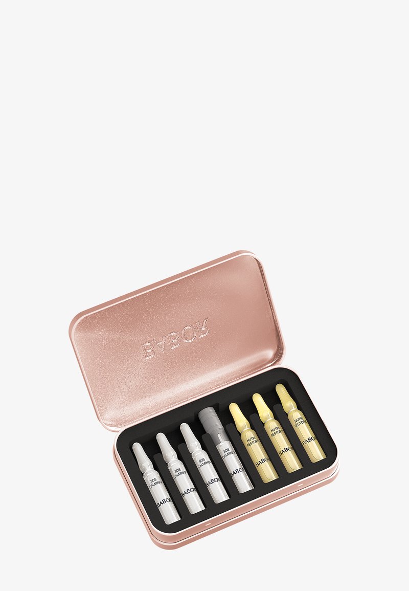 Boîte en or rose métallique contenant huit ampoules de soins de la peau dans une mousse noire, quatre étiquetées SOS Calming et quatre étiquetées Nutri Restore.