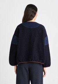 Pullover in misto lana blu navy con maniche a palloncino, caratterizzato da un colletto a contrasto e dettagli a forma di diamante sulle maniche. Dettagli a coste sull'orlo.