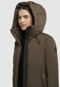 Brown padded jacket with a large hood, featuring a front zipper, snap buttons, and side pockets. Smooth texture and adjustable drawstring.