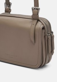 Beżowa skórzana torba na ramię o strukturalnym kształcie, z podwójnym zamknięciem na zamek błyskawiczny oraz srebrnymi akcentami. Posiada widoczne detale w postaci przeszyć.